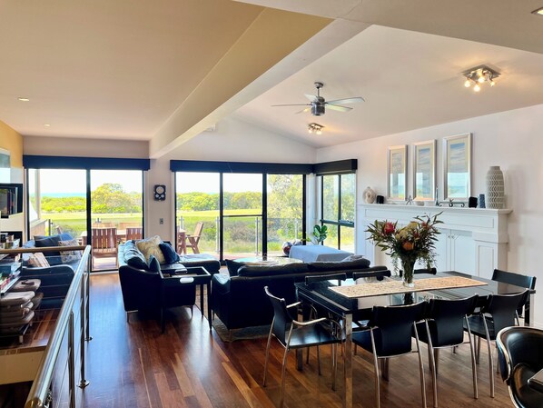 A spacious living area with a large window, a ceiling fan, and a fireplace. - Top Views Retreat: 5 BR, 3 BA House in Torquay, Sleeps 11 (Torquay)