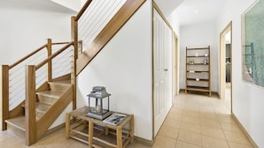 A wooden staircase with a lantern on a woven stool, a white door, and a bookshelf in a hallway with tiled flooring. - Whites Retreat (The Esplanade) (Torquay)