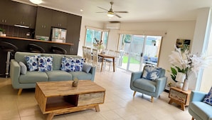 A modern living room with a sofa, armchairs, and a coffee table. There is a kitchen area with cabinets and a dining table. - Whites Retreat (The Esplanade) (Torquay)
