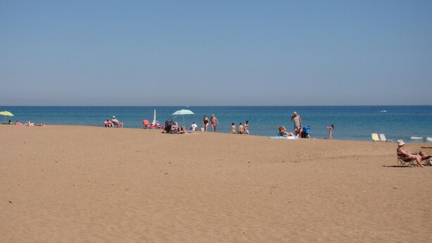 A beach with people sunbathing and swimming, umbrellas, and a clear blue sky.