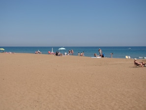 A beach with people sunbathing and swimming, umbrellas, and a clear blue sky. - Ideal apartment for families with playground, pool and garden (Denia)