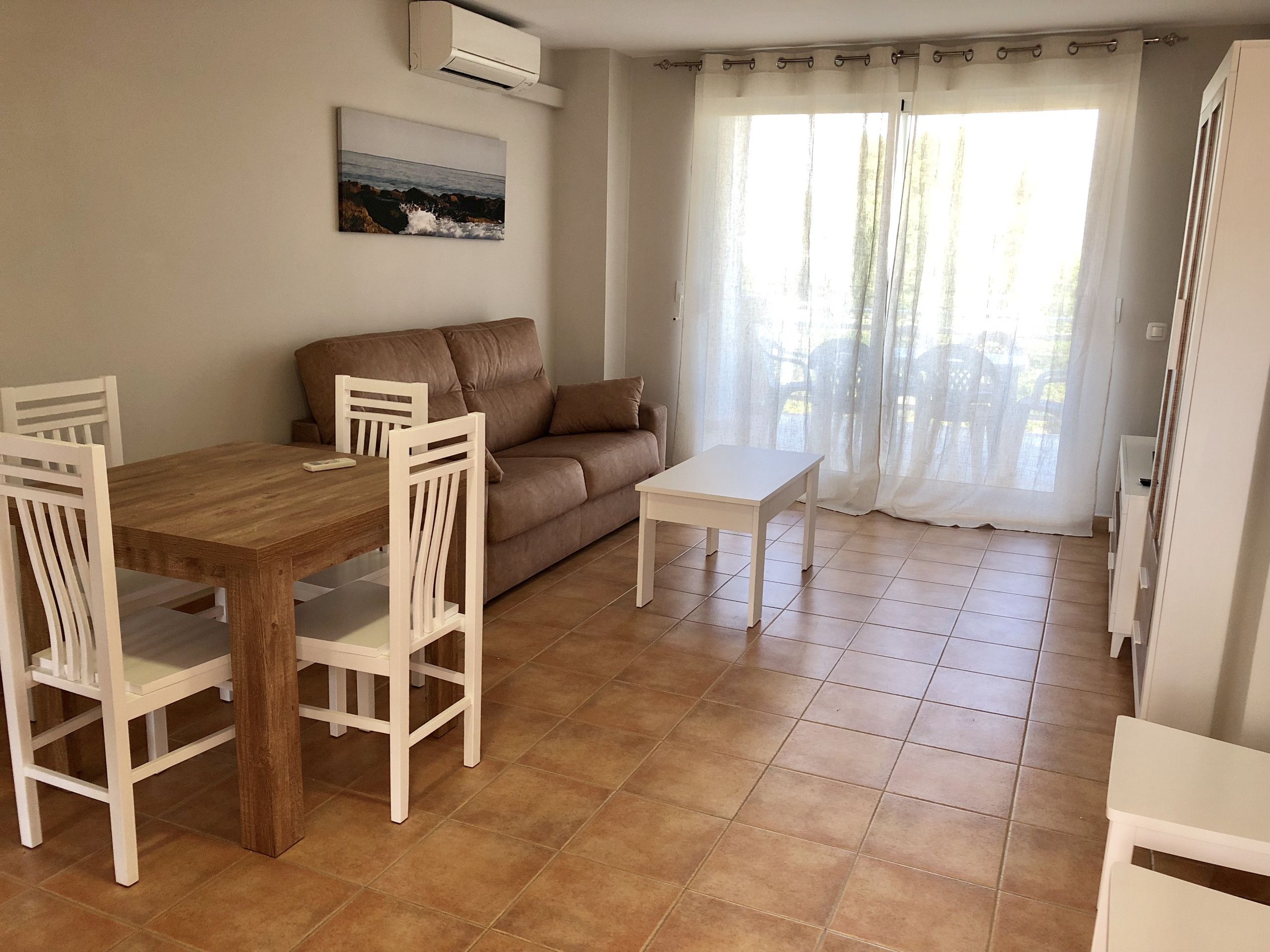 A dining area with a wooden table and white chairs, a brown sofa, and a white coffee table.