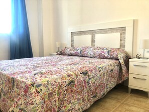 Une chambre à coucher avec une couvre-lit à motifs floraux, une tête de lit en bois, une table de chevet avec une lampe et une petite table de nuit.