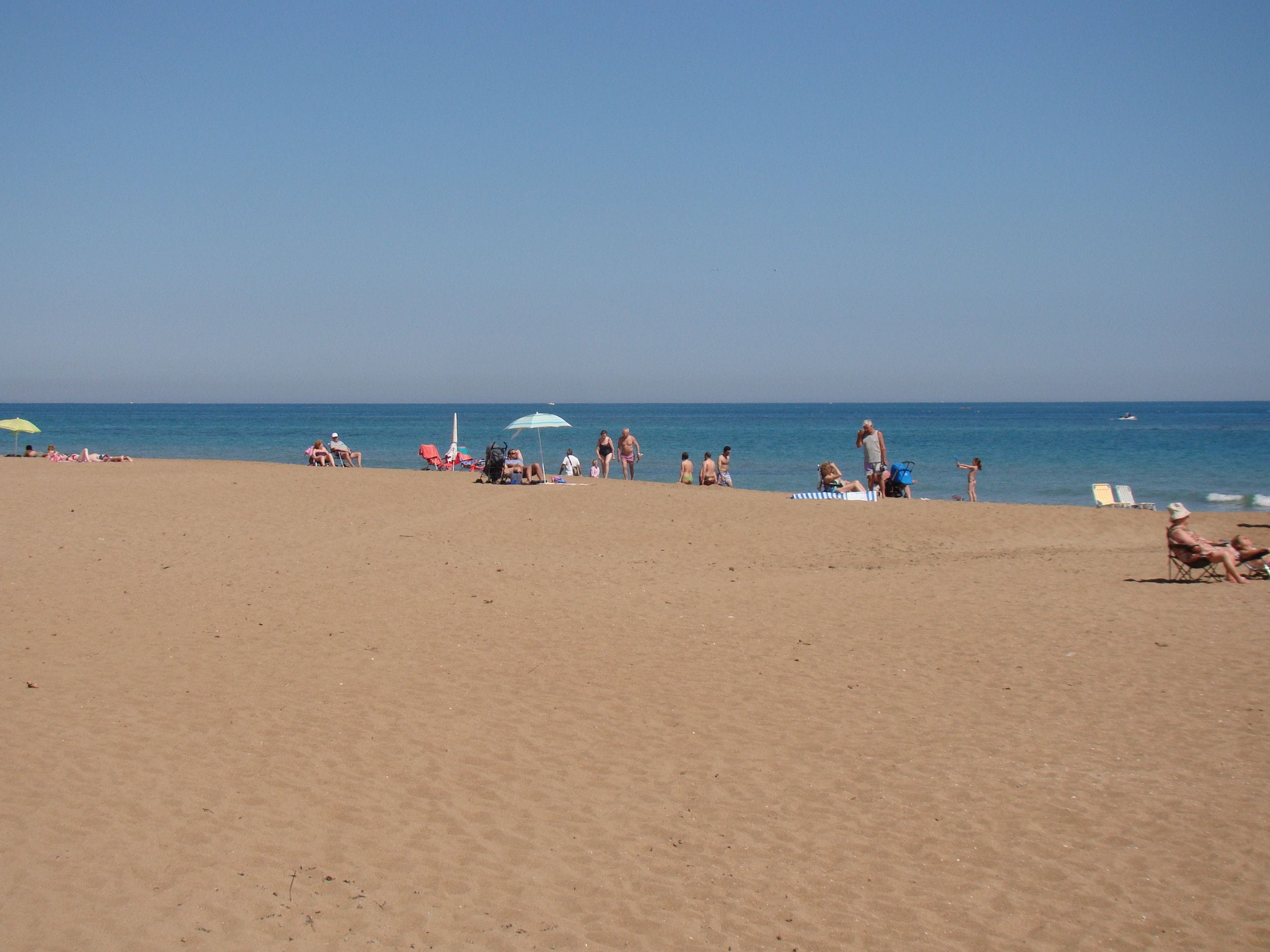 Une plage où l’on peut voir des gens se prélasser au soleil et nager, des parasols et un ciel bleu dégagé.