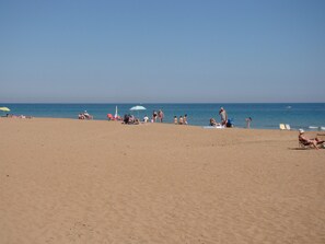 A beach with people sunbathing and swimming, umbrellas, and a clear blue sky. - Ideal apartment for families with playground, pool and garden (Denia)