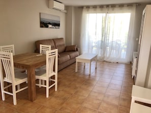 A dining area with a wooden table and white chairs, a brown sofa, and a white coffee table. - Ideal apartment for families with playground, pool and garden (Denia)