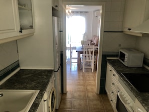A kitchen with a washing machine, microwave, and a dining area with chairs and a table.
