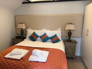 A neatly made bed with white linens and decorative pillows, two bedside tables with lamps, and a patterned bedspread. - Artists' Cottages (Harrogate)