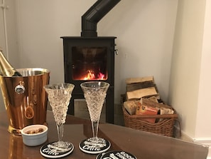 Un cuarto acogedor con una estufa de leña, dos vasos de cristal, un cántaro de cobre y una cesta de leña.