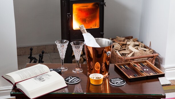 Una mesa de madera con un libro, dos vasos de cristal, un coctelero de cobre y una bandeja con tachuelas de madera.