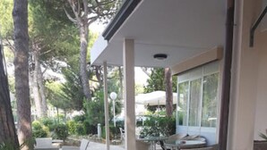 An outdoor seating area with white chairs and a round planter with pink flowers. - Elsa (Cervia)