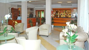 A lobby with a reception desk, seating area with chairs and tables, and a bar with bottles. - Elsa (Cervia)