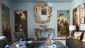 A room with a green armchair, a black sofa, a round coffee table, and a decorative mirror.