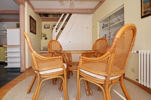 A dining area with a round table and four wicker chairs, a staircase in the background, and a radiator on the wall. - Cozy vacation apartment in Ahlbeck with a small garden - only 400 m to the beach! (Seebad Ahlbeck)