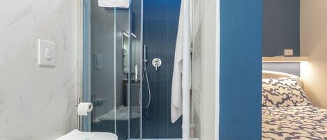 Un baño moderno con ducha envuelta en vidrio, inodoro y cama con ropa de cama estampada.