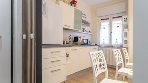 A modern kitchen with white cabinets, a microwave, and a sink. There are white chairs and a table in the dining area. - B&B Pensieri D'Autore (Campobasso)