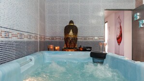 Een spa-ruimte met een groot bad, een Boeddha-beeld en een muur met een mozaïekpatroon.