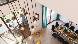 Een moderne eetruimte met een hoge plafond, hanglampen en uitzicht op de omgeving.