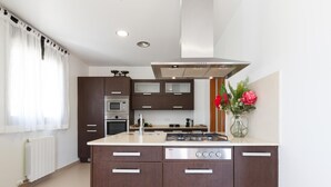 Een moderne keuken met een centraal eiland, roestvrijstalen apparatuur en een raam met transparante gordijnen.