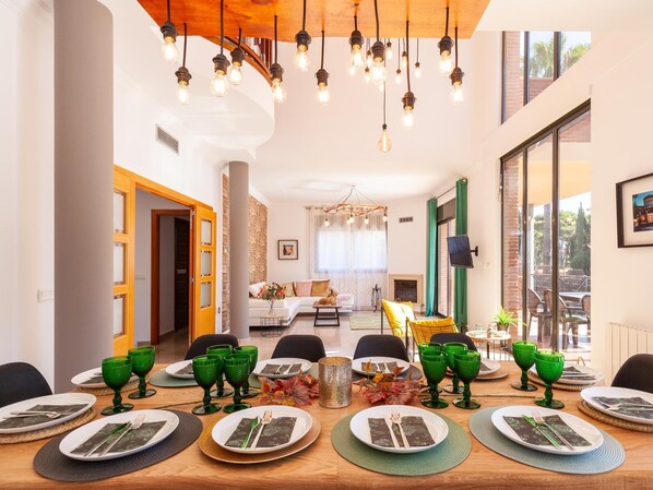 A dining area with a long table set for six, green glassware, and a modern chandelier.