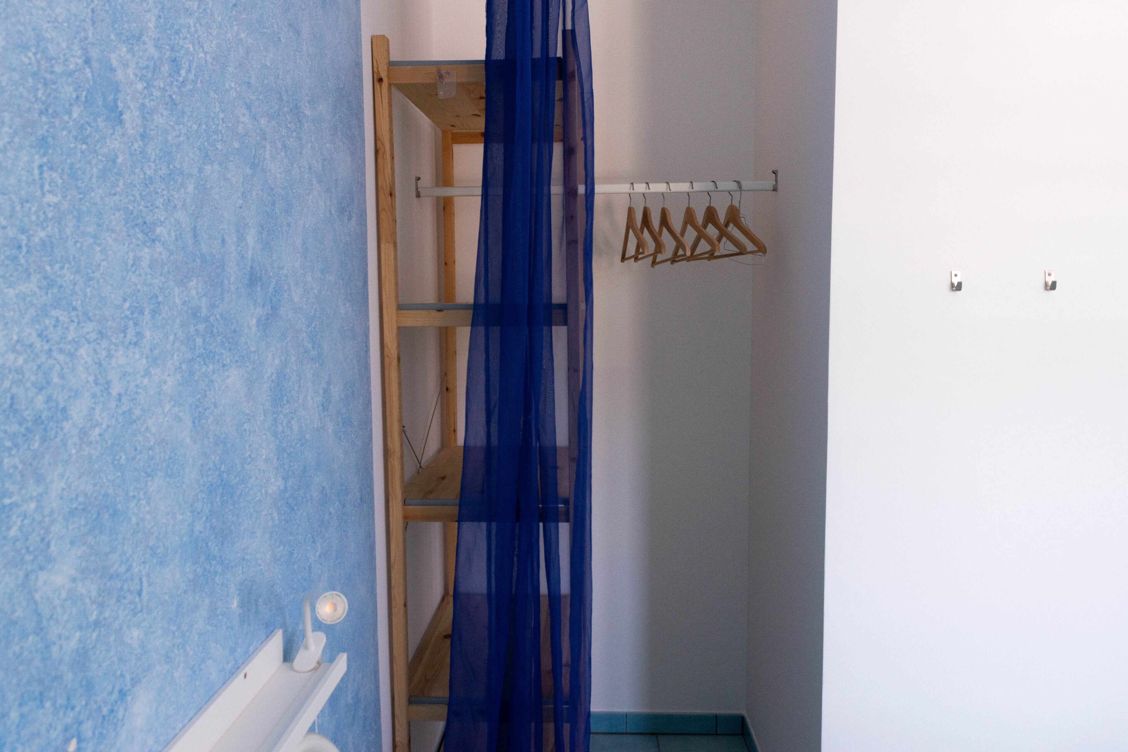 Una habitación con pared azul con textura, un estante de madera y una cortina translúcida azul.