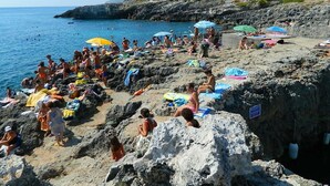 Ein felsiger Strand mit badenden und sonnenden Personen.