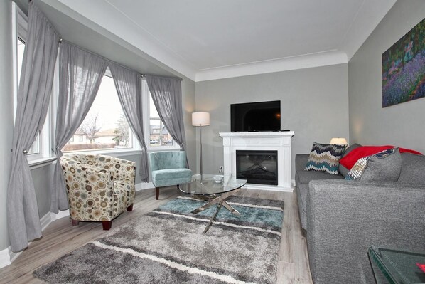 A living room with a fireplace, a sofa, a patterned armchair, and a glass coffee table.