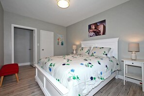 A bedroom with a large bed, a nightstand, a red chair, and a door.