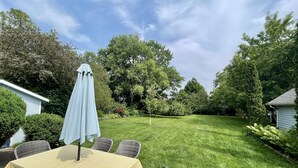 Eine Terrasse mit Tisch und Stühlen, umgeben von einem gepflegten Rasen und Bäumen.