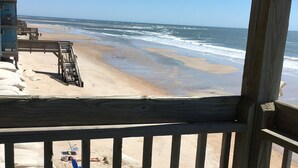 Vista a la playa desde una terraza de madera, con una silla y una mesita.