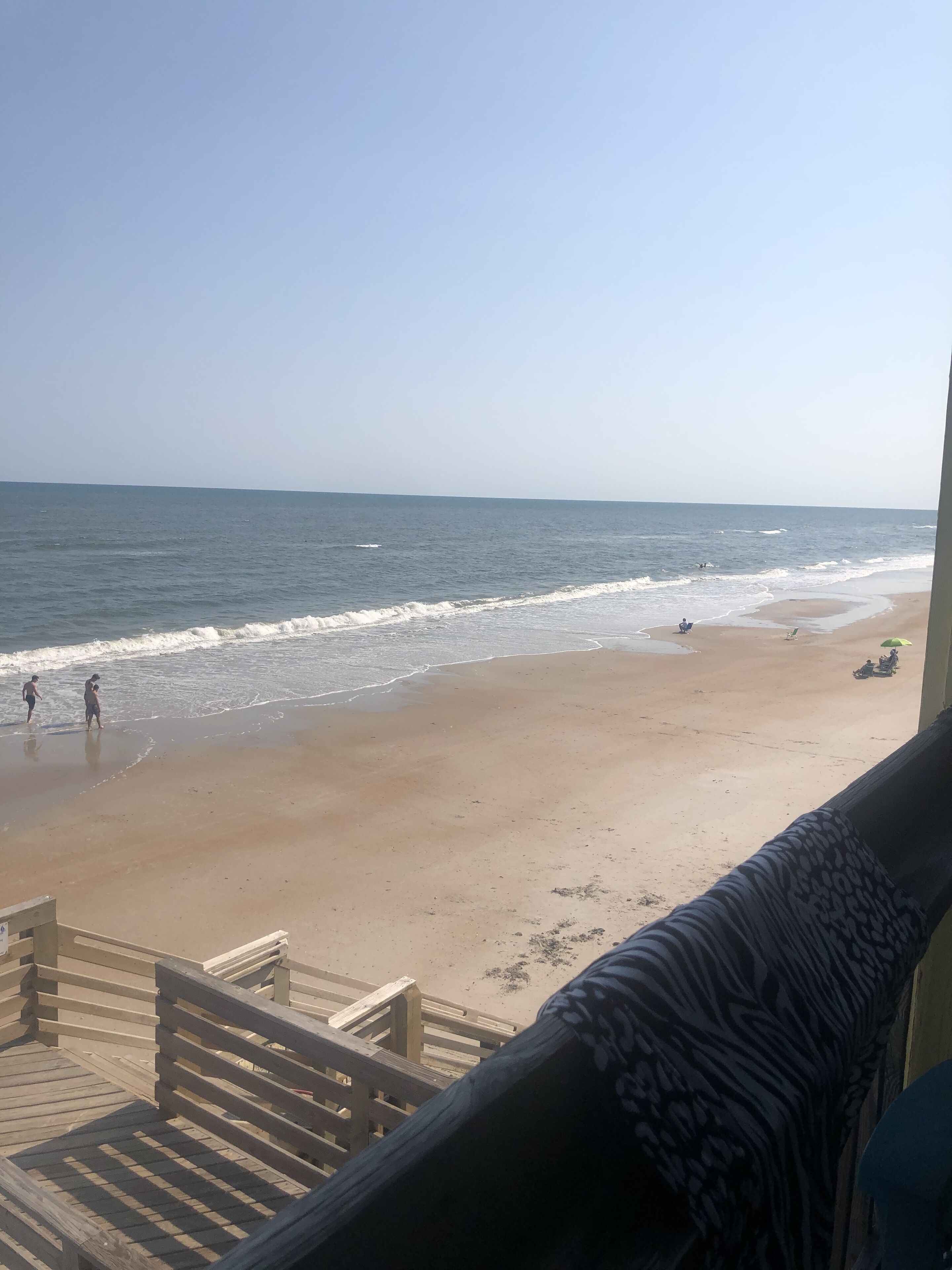 Blick auf den Strand vom Balkon mit Holzgeländern und einem gemusterten Kissen.