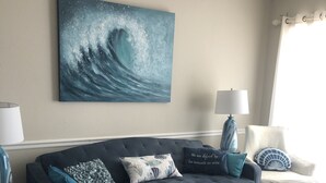Un salón con un sofá azul oscuro, un reposapiés estampado y un cuadro grande con forma de ola en la pared.
