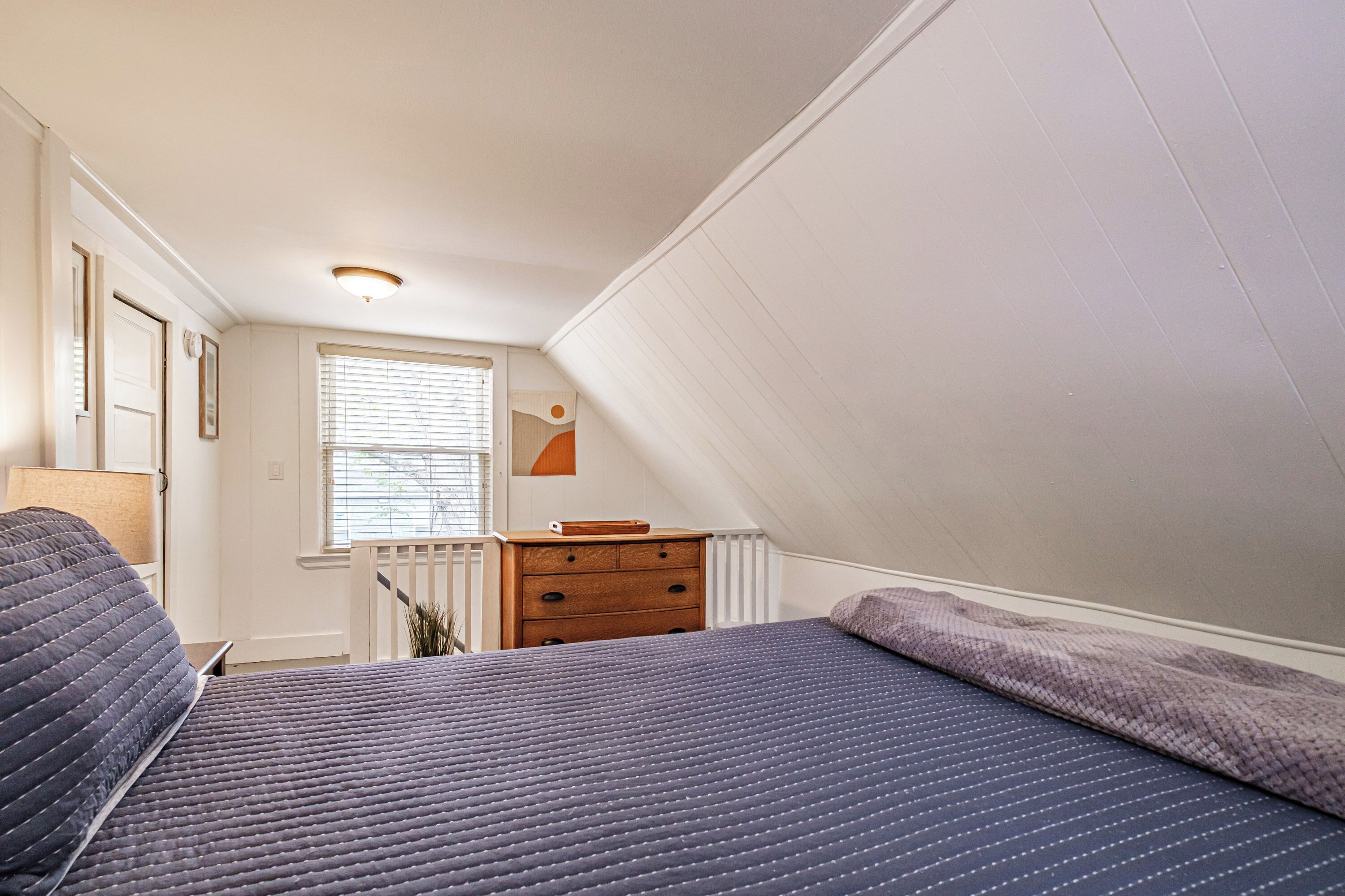 A bedroom with a bed, dresser, and window with blinds.