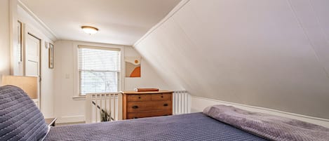 Ein Schlafzimmer mit Bett, Kommode und Fenster mit Jalousien.