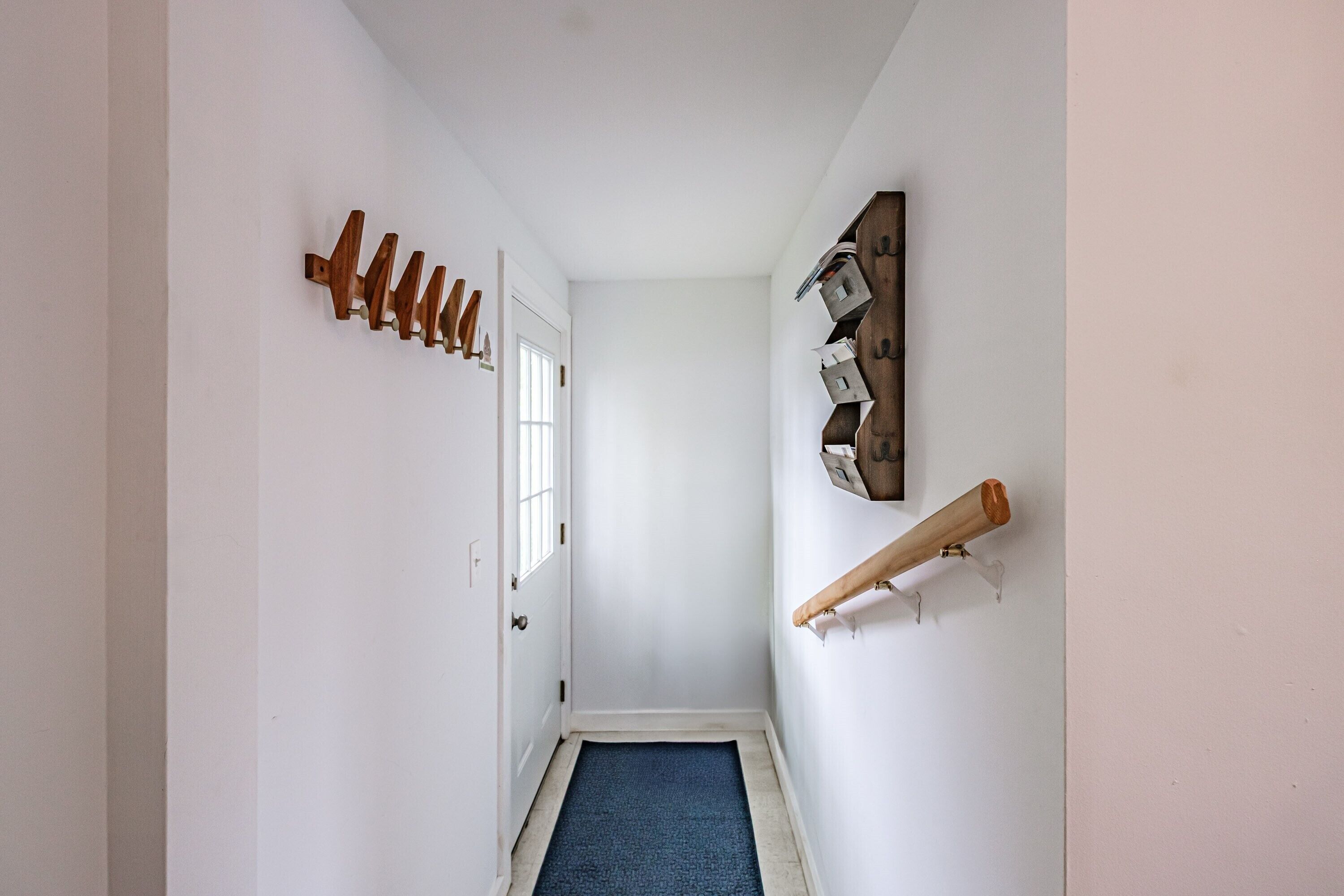 A narrow hallway with a blue carpet, a wooden coat rack, and a wall-mounted shelf.