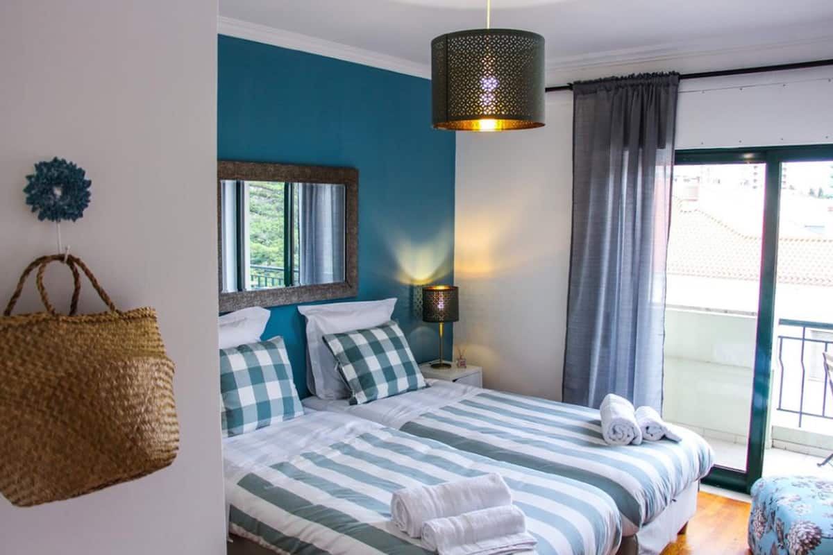 A bedroom with a bed, a hanging lamp, a window, and a balcony door.