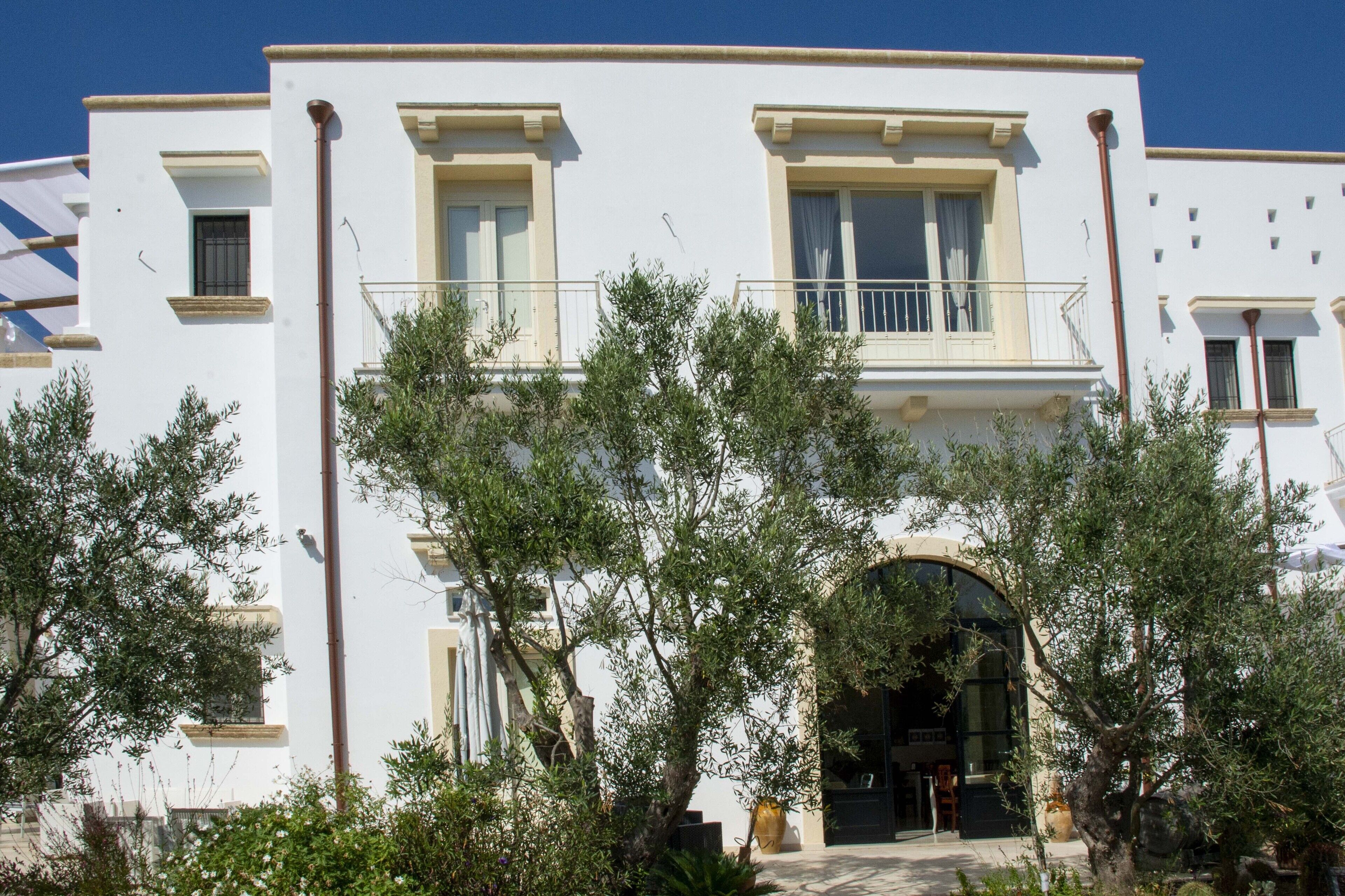 Un edificio blanco con balcón, rodeado de árboles.
