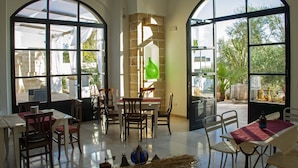 A spacious dining area with large arched windows, a central table with chairs, and a stone accent wall. - Casale Donna Rosa (Sannicola)
