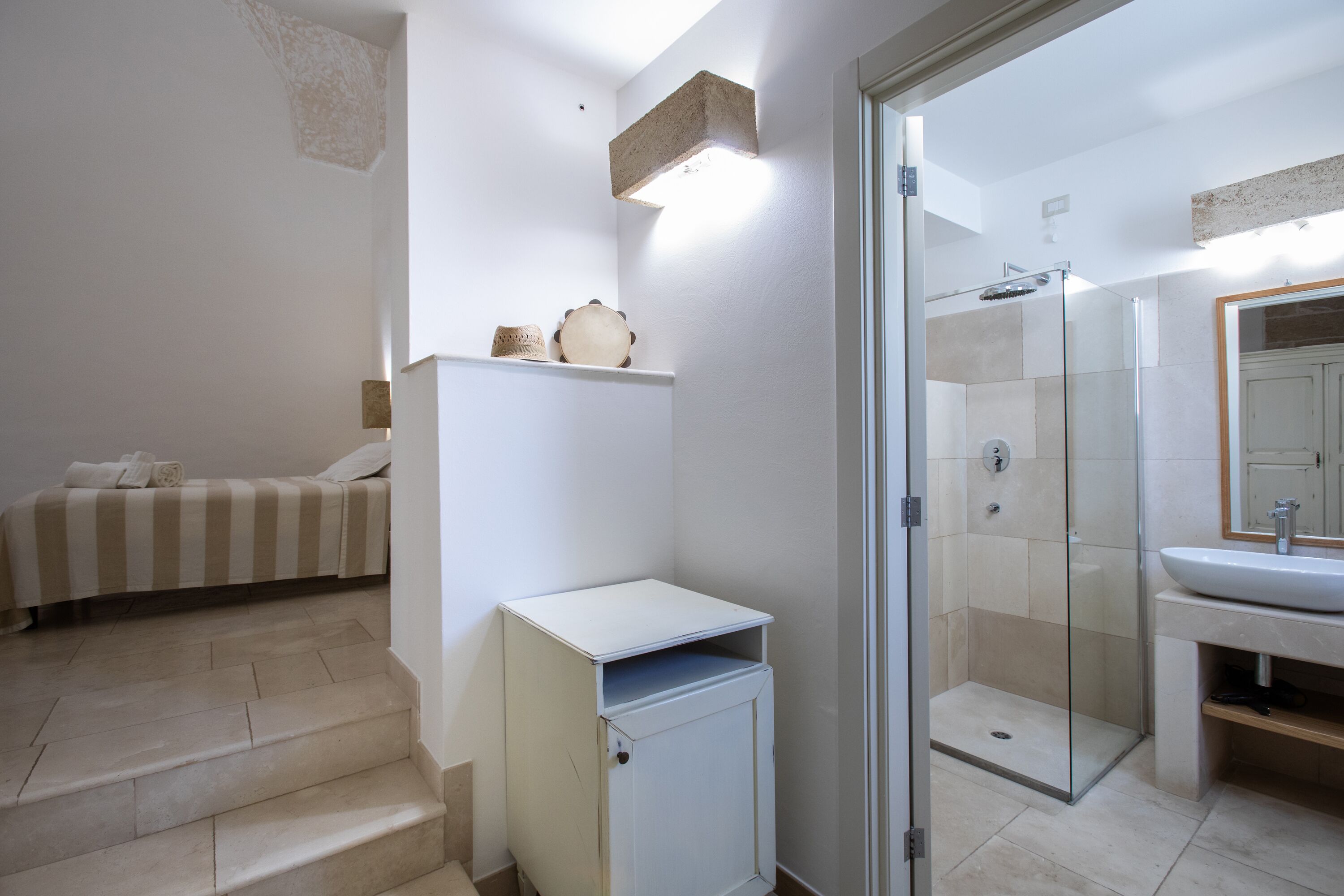Une salle de bain moderne avec une douche en verre, un lavabo blanc et un lit avec une literie à rayures.