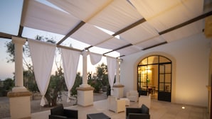 An outdoor patio area with seating arrangements, a covered section with a view of the landscape, and a building entrance. - Casale Donna Rosa (Sannicola)