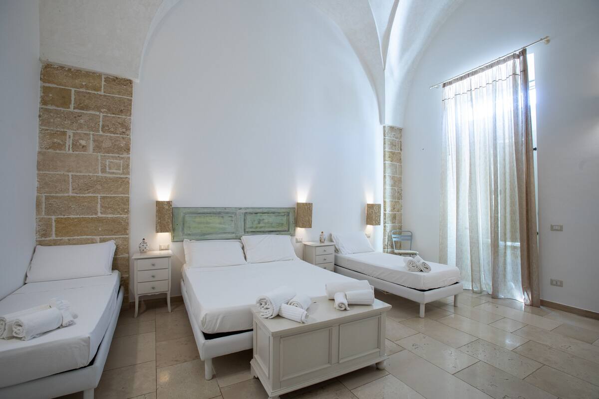 A hotel room with three beds, a large mirror, and a stone wall.