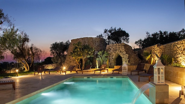 A swimming pool with a stone structure in the background, surrounded by lounge chairs and a stone wall. - Casale Donna Rosa (Sannicola)