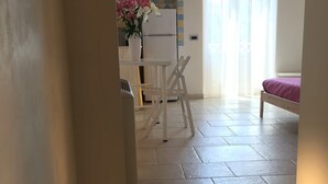 Una cocina moderna con un refrigerador blanco, una mesa de comedor con sillas y una ventana con cortinas traslúcidas.