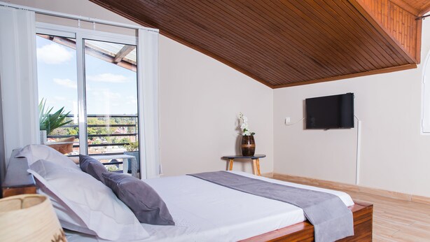 Ein Schlafzimmer mit einem Holzbett, einem Fernseher an der Wand und Blick ins Freie.