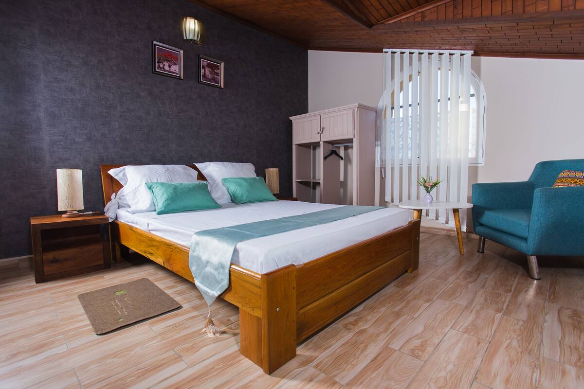 A bedroom with a wooden bed, a nightstand, a wardrobe, a chair, and a small table with a plant.
