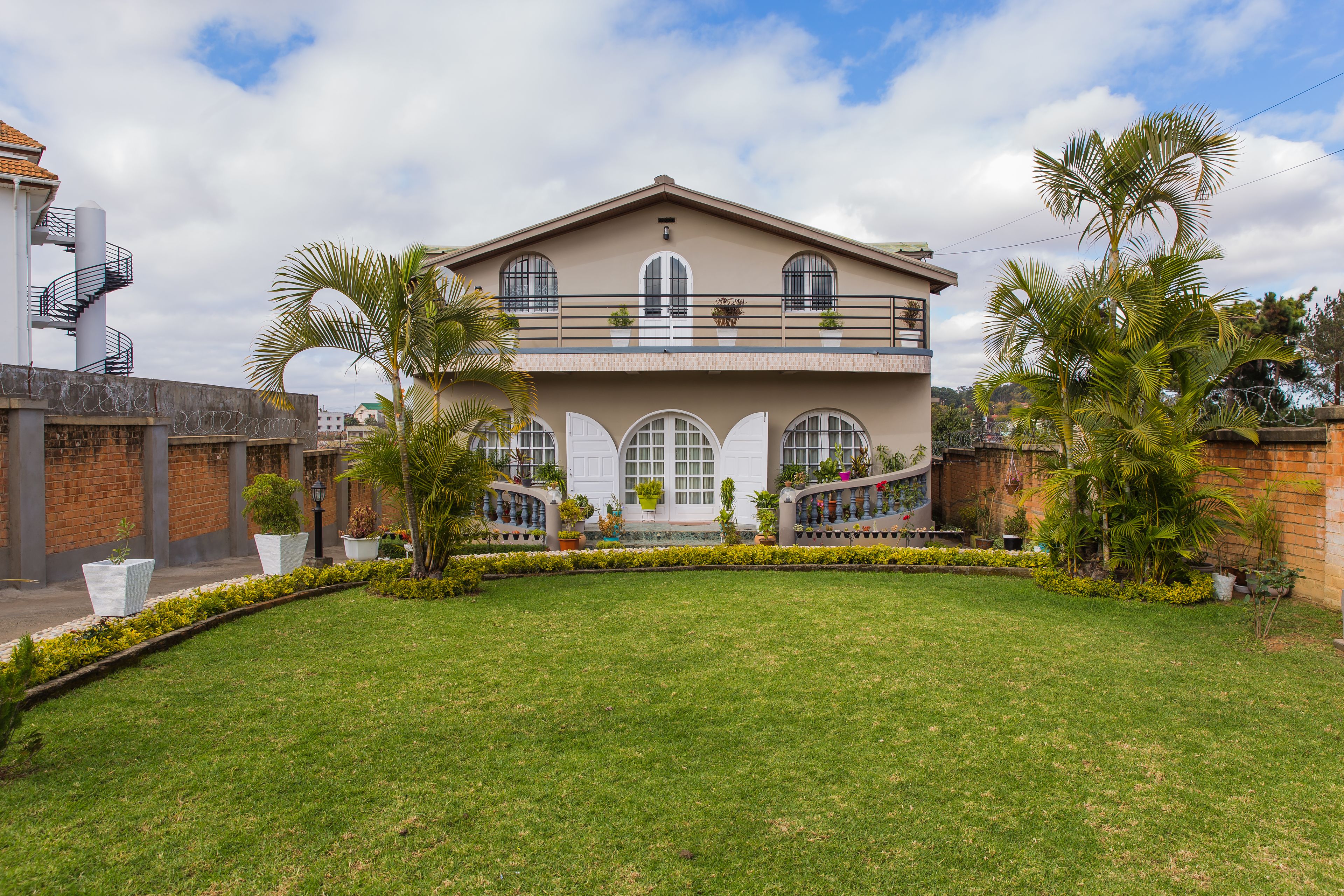 A two-story building with a balcony, surrounded by a well-maintained lawn and palm trees.