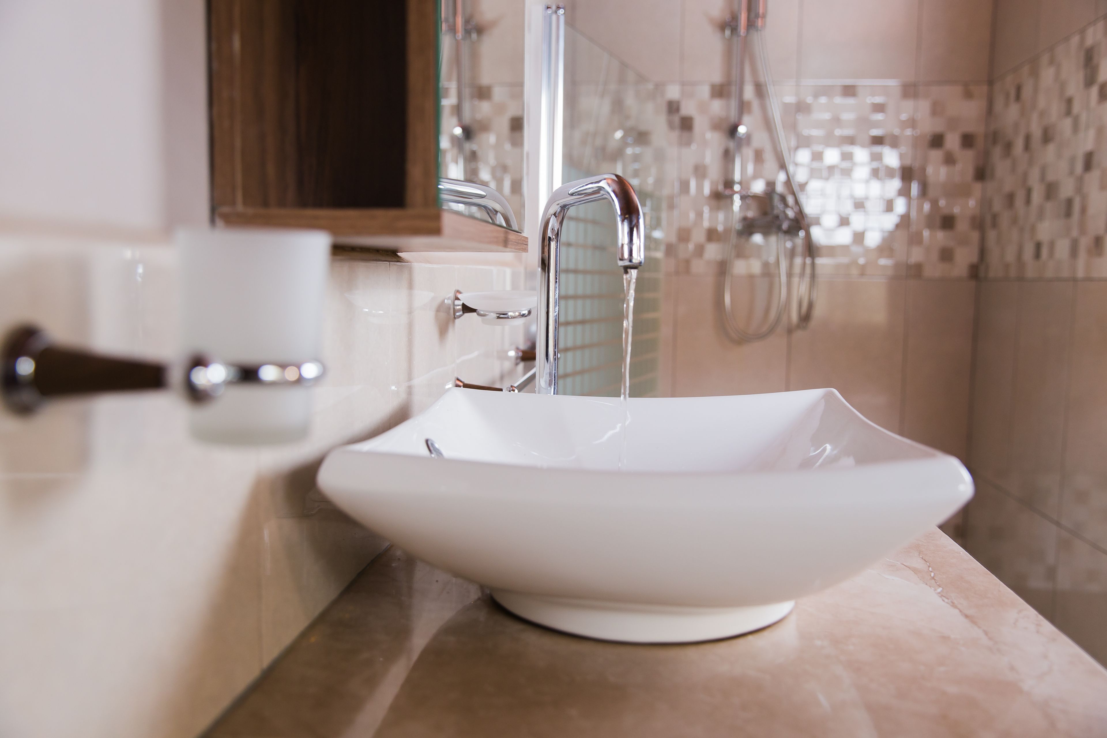 Une salle de bain moderne avec un lavabo sur colonne blanc, une douchette à main et une douche à parois de verre.