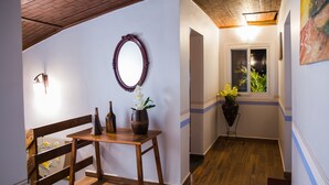 Ein Flur mit Holzboden, einer Holzbank, einem Tisch mit Blumenvase, einem Spiegel an der Wand und einem Fenster mit Blick ins Grüne.