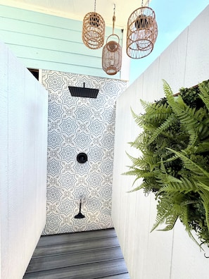 A narrow hallway with patterned wall tiles, a wooden floor, hanging wicker lamps, and a large fern plant.