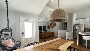 A dining area with a wooden table and chairs, a hanging chair, and a kitchen in the background.